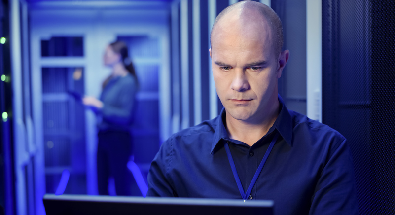 Male IT engineer using laptop in server room.